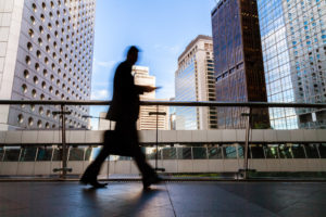 A blurred silhouette of a man walking down a walkway with a cityscape in the background.